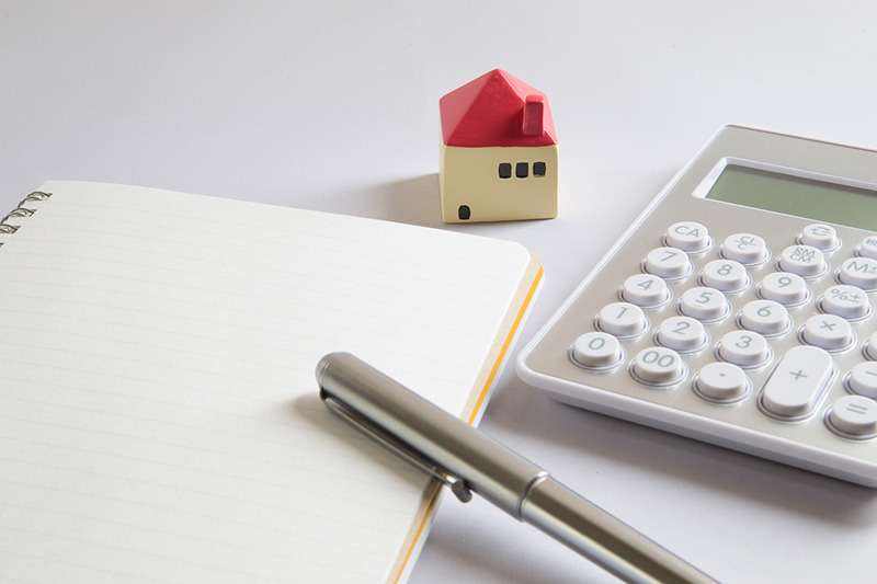 赤い屋根の小さな家の模型と、ノート、ペン、電卓